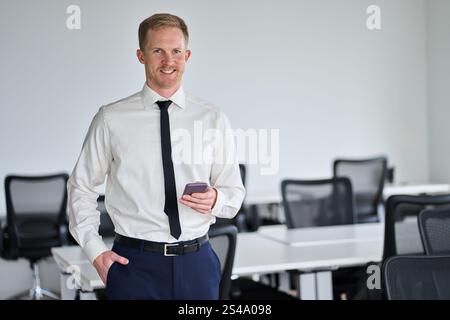 Happy confident young businessman using smartphone in office. Portrait. Stock Photo
