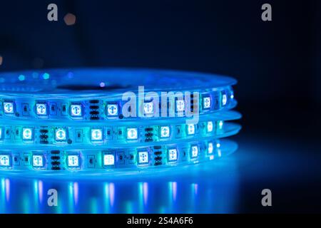 Bobbin with roll of glowing LED strip lighting placed on table, blue color in dark room Stock Photo