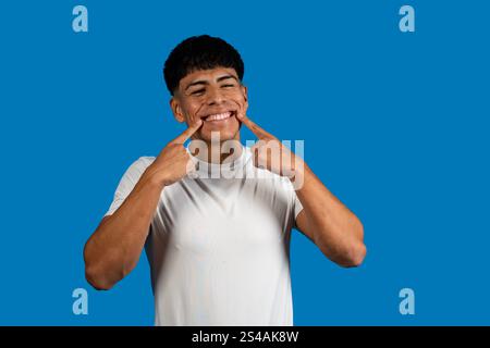 Happy latin man pointing his perfect smile with fingers on a blue background Stock Photo