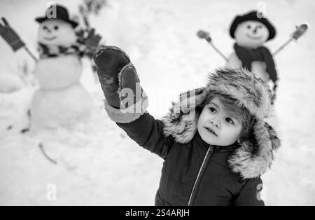 Child boy Having Fun in Winter Park. Winter clothes for kids. Happy winter time. Beauty child with snowman in frosty winter Park. Stock Photo