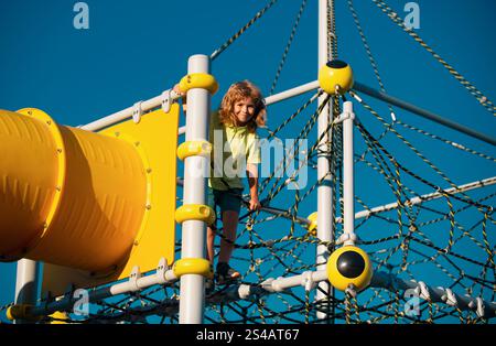 School kid climbing in the school playground. Cute and happy little child boy climbed on top of the rope web, kids growth concept. Funny kids face. Stock Photo