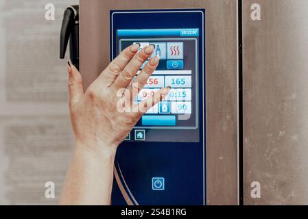 Utility worker in restaurant pressing buttons on refrigerator control panel, cook freezing food Stock Photo
