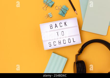 Back to school. Lightbox with letters, headphones and stationery on a yellow background. Place for your design. Stock Photo