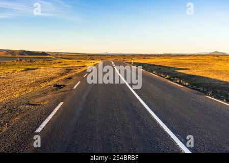 Empty road warmly lit by midnight sun in Iceland in summer Stock Photo