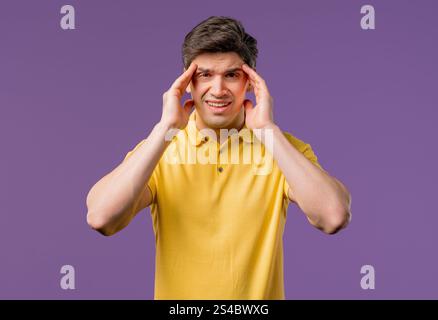 Young man having headache, blood pressure, studio portrait. Guy putting hands on head, isolated on violet background. Concept of problems, medicine, i Stock Photo
