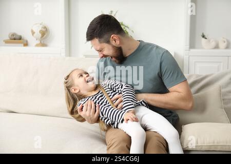 Happy father and his cute little daughter on sofa at home Stock Photo