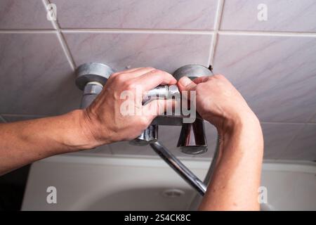 Woman changing broken shower hose in bathroom. Female plumber hands fixing hose. Plumbing concept. Male and female professions concept. Stock Photo