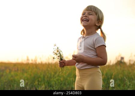 Cute little girl with chamomiles at meadow, space for text. Child enjoying beautiful nature Stock Photo