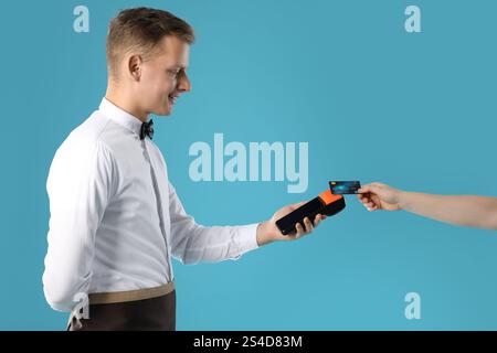 Waiter taking payment from client via terminal on light blue background Stock Photo