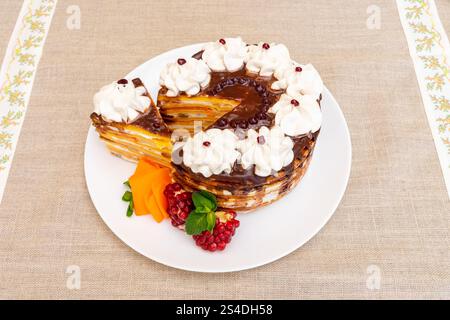 A beautifully crafted multi-layered cake is presented on a white plate, topped with whipped cream and contrasting fruits. The setting features a light Stock Photo