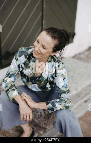Smiling, dark-haired woman, 40+, sitting on a staircase Stock Photo