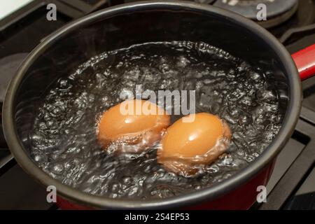 Two orange eggs boiling in a  black pot with bubbles and steam Stock Photo