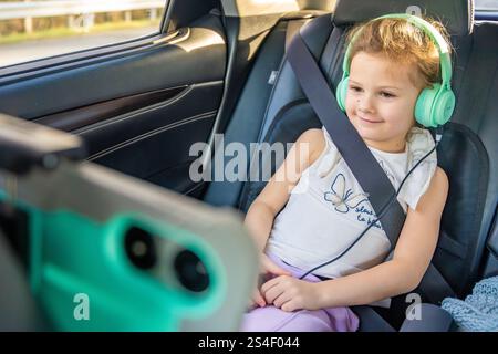 Little girl with tablet and headphones in the car during travel on vacation. Entertainment in the transport for child Stock Photo