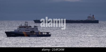 Sassnitz, Germany. 12th Jan, 2025. The unmaneuverable tanker "Eventin" is lying in the Sassnitz roadstead between Binz and Sassnitz. The tanker, loaded with around 99,000 tons of oil, is to remain there until a decision has been made on how to proceed. The federal police vessel BP82 "Bamberg" sails in front of the oil tanker. Credit: Stefan Sauer/dpa/Alamy Live News Stock Photo