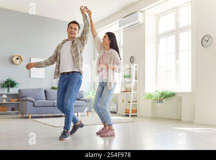 Happy laughing young couple having fun dancing at home in living room. Stock Photo