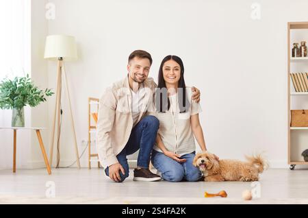 Portrait of happy young family couple with adorable fluffy pet dog on floor at home Stock Photo