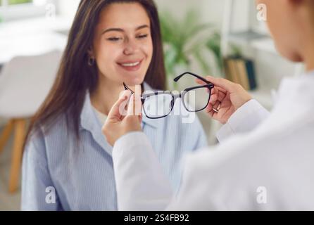 Young smiling woman trying on new eyeglasses in medical clinic or optical store to improve vision. Stock Photo