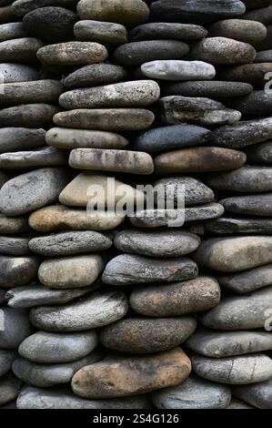 Background walls - Pebbles or river stones stacked on top of each other to form a pyramid, natural stone wall in gardening texture. Stock Photo