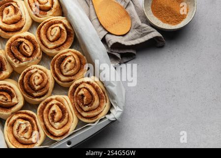 Raw cinnamon rolls sprinkled with cinnamon powder, prepared for baking, with brown sugar and wooden spoon Stock Photo