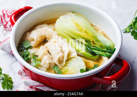 Gyoza soup with mushroom broth and bok choy in a red pot, close-up. Japanese cuisine concept. Stock Photo