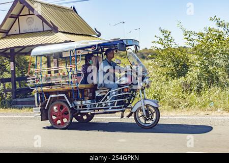 UBON RATCHATHANI, THAILAND, DEC 17 2024, A traditional motorized tricycle taxi is driving along a rural road Stock Photo