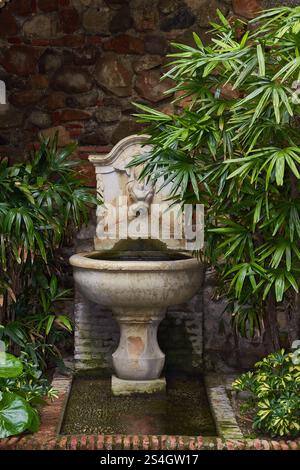 Decorative Garden Fountain Surrounded by Lush Green Plants and Stone Wall at Gibralfaro Castle, Malaga, Spain,. Stock Photo