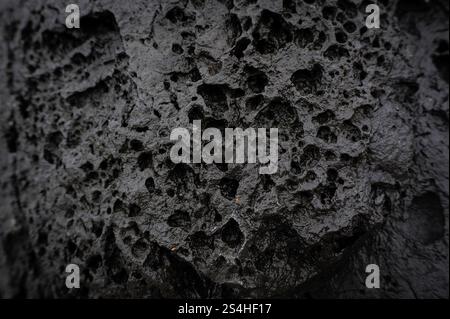 Black grey background lava stone with erosion holes caused by wind, water and weather. Backdrop surface weathered grunge and furrowed. Stock Photo