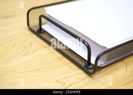 Metal black paper tray with white empty sheets of A4 paper on light wooden desk. Office work, documents and paperwork at workplace Stock Photo
