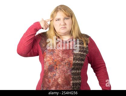 A middle-aged woman expressing frustration by pointing at her head. She is wearing a red patterned sweater and has a serious expression on her face. Stock Photo