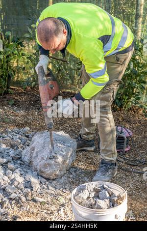 A worker smashes a large concrete block using an electric demolition hammer Stock Photo