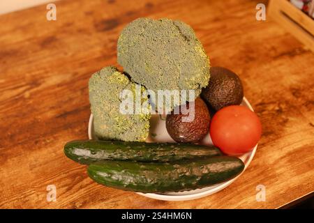 Fresh vegetables and fruits arranged on a plate in a rustic kitchen setting Stock Photo