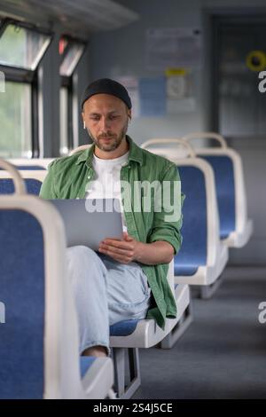 Focused thoughtful man passenger working on laptop while travel by electric train using earphones  Stock Photo