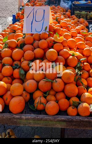 A pile of oranges with a sign that says 19. The oranges are piled high on a wooden table Stock Photo