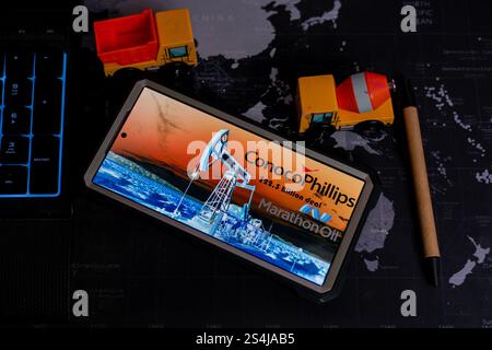 Smartphone displaying ConocoPhillips's acquisition of Marathon Oil, positioned on a world map, alongside toy trucks and a pen, symbolizing global ener Stock Photo