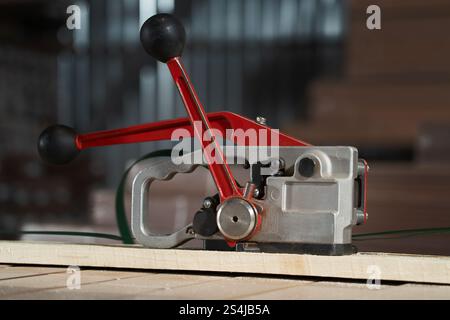 Manual belt tensioner on a wooden surface in an industrial area. Tool for working with packaging. Stock Photo