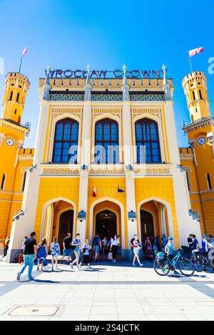 The grand Neo-Gothic facade of Wroclaw Główny railway station, with ornate architecture and clock tower against a blue sky.