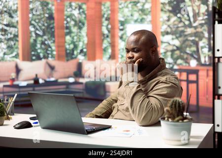 Freelancer at desk conducting business analysis and creating detailed financial reports on a modern laptop. Remote working professional managing projects from his home office. Stock Photo