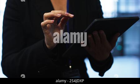 Programmer managing data center with advanced technology using digital device. Close up shot of woman walking in server room, optimizing data center tech with tablet, camera A Stock Photo