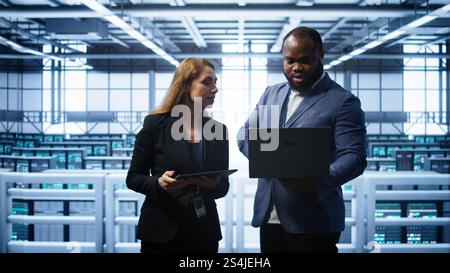 African american admin greeting inspector arriving in data center to supervise operations. IT expert in server hub workspace doing hand shake with supervisor monitoring performance, camera B Stock Photo