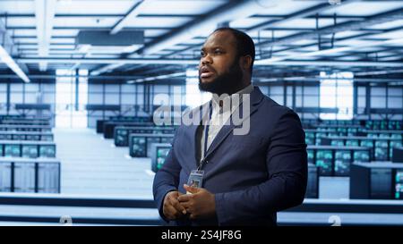 System administrator looking at holograms in data center, monitoring equipment. Employee in server farm interacting with futuristic augmented reality AI visualization, camera A Stock Photo