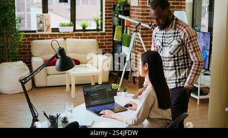 Diverse software developers team coding on a laptop in a cozy home office, working on a new program or app development. Specialists in IT promote programming language and remote tech work. Camera A. Stock Photo