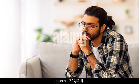 Pensive arab guy sitting on couch at home Stock Photo