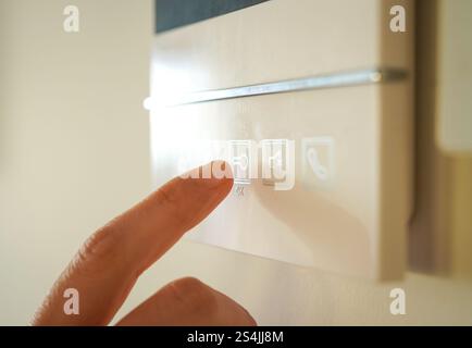 Intercom, TV door phone linked to electric lock Close-up of woman's hand trying to press button to unlock door Stock Photo