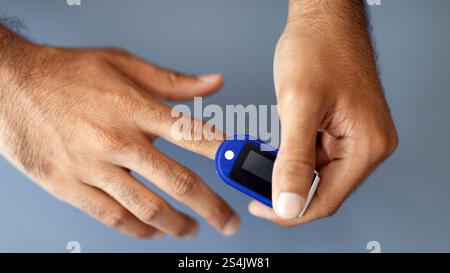 Unrecognizable man using pulse oximeter, grey background Stock Photo
