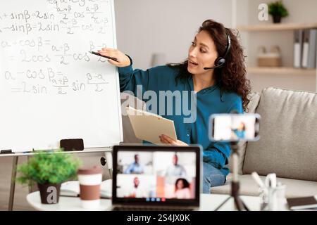 Lady teacher in headset explaining trigonometric functions to students online Stock Photo