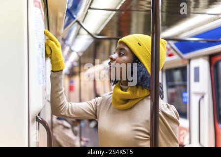 Tourist wearing yellow winter clothes checking subway map while traveling inside metro train Stock Photo