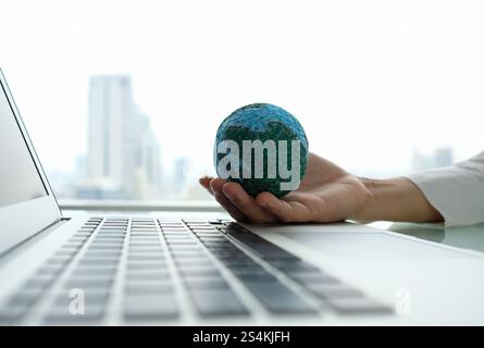 global of technology and business concept. globe on hand and laptop computer with business city background. Stock Photo