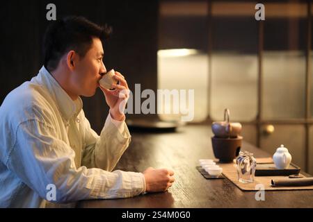Chinese young man holding teacup drinking tea. Side view Stock Photo