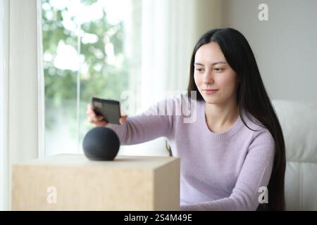 Asian woman pairing phone with smart speaker sitting on a couch at home Stock Photo