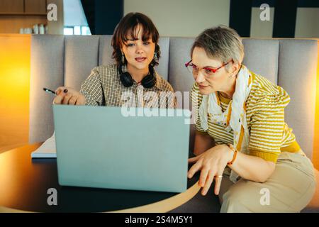 Two colleagues of different ages collaborating on a project using a laptop, showcasing diversity and teamwork in a professional environment. Stock Photo